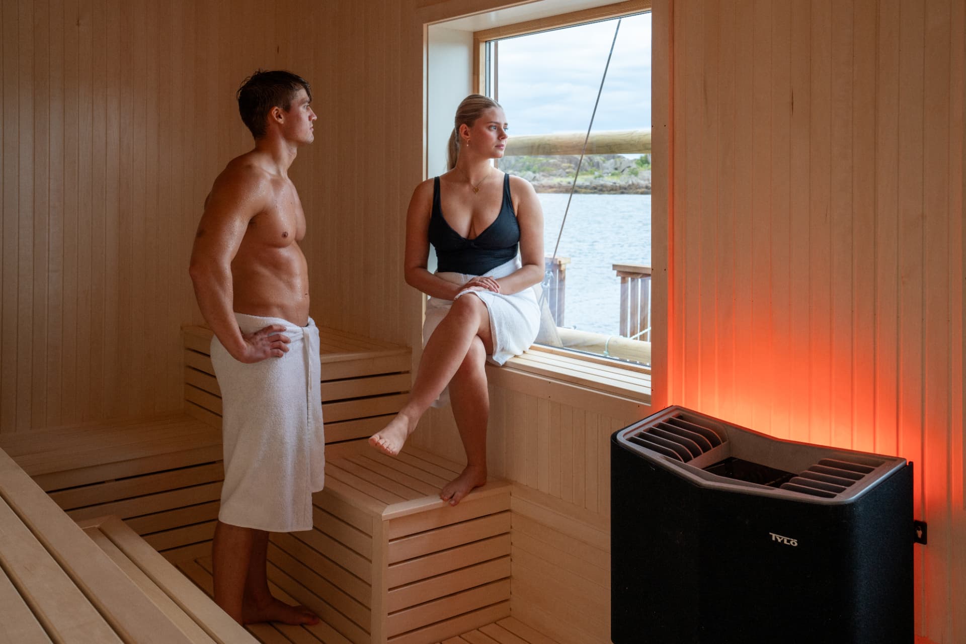 Guests in the URE sauna looking out over the sea through a wide window