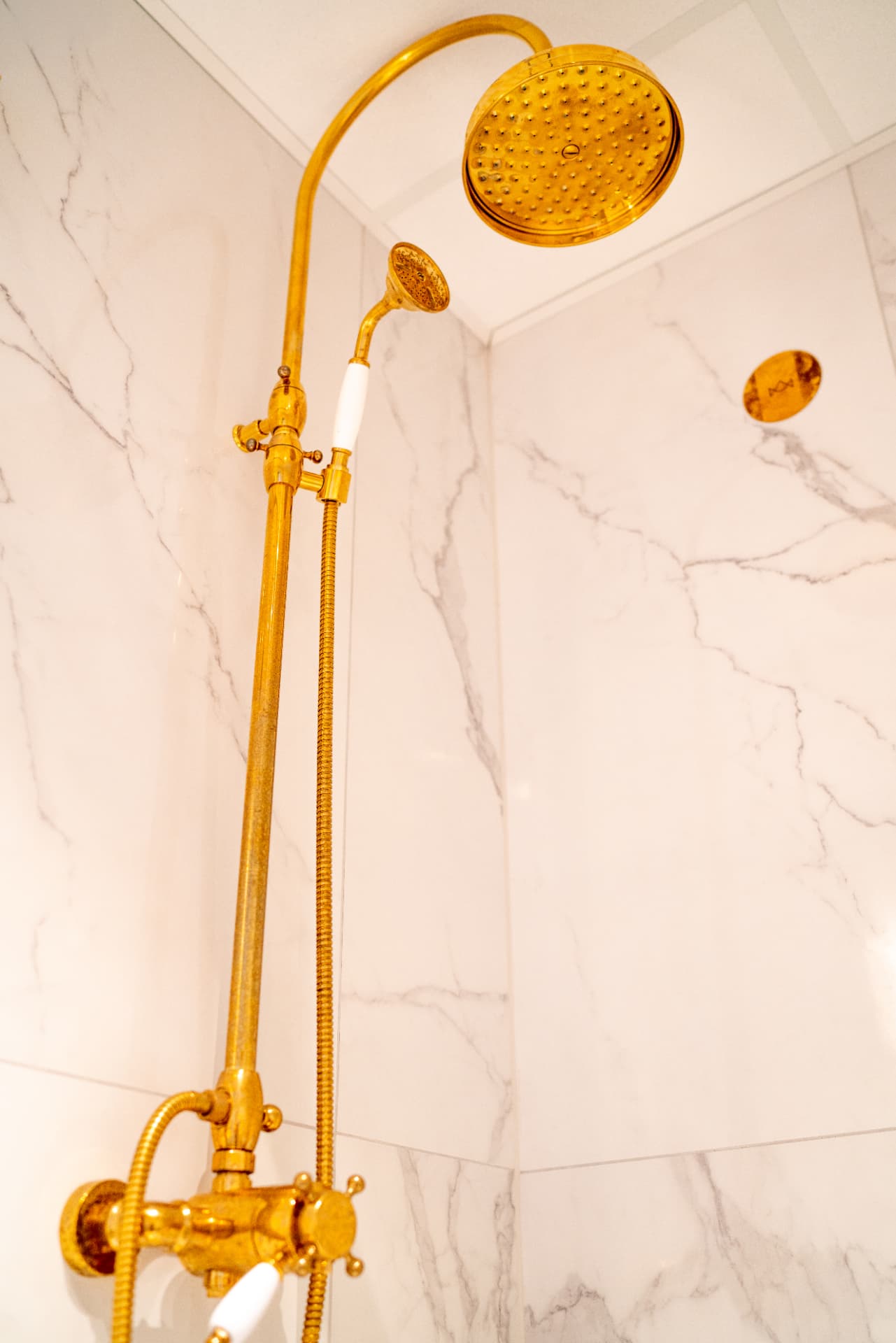 URE bathroom — brass rainfall shower against marble tiling